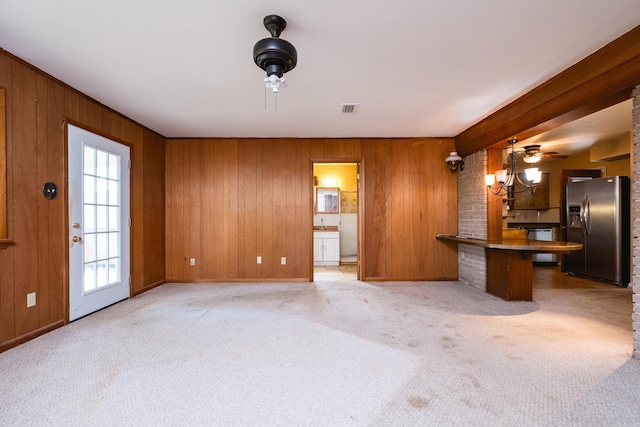 unfurnished living room featuring wooden walls, visible vents, baseboards, and light colored carpet