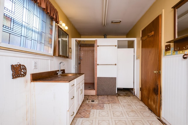 kitchen featuring visible vents, a sink, dark countertops, white cabinetry, and a wainscoted wall