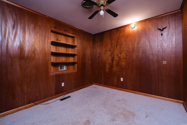 empty room with wooden walls, visible vents, a ceiling fan, and carpet flooring