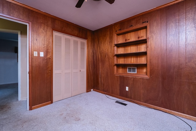 unfurnished bedroom featuring a closet, carpet flooring, wood walls, visible vents, and ceiling fan