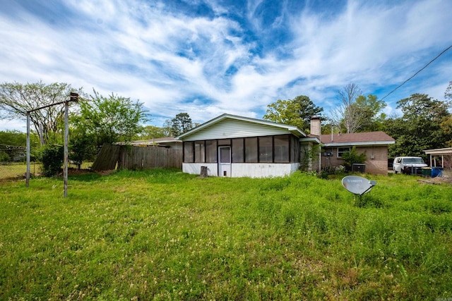 rear view of house featuring a sunroom, a chimney, fence, and a lawn