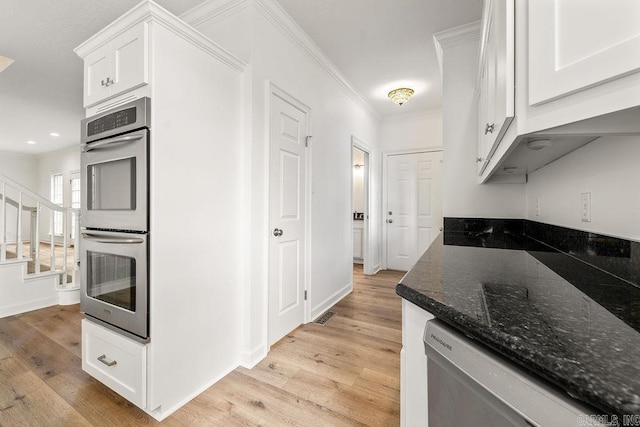 kitchen featuring stainless steel appliances, light wood-style flooring, white cabinets, dark stone countertops, and crown molding