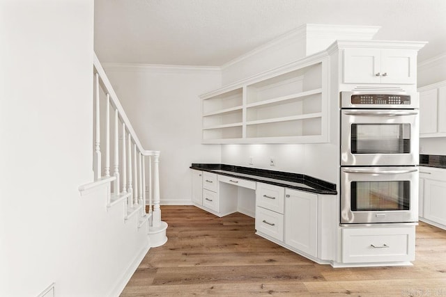 kitchen featuring double oven, open shelves, ornamental molding, dark countertops, and light wood-type flooring