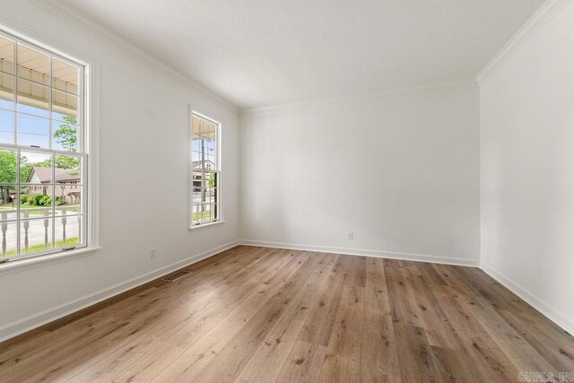 empty room featuring healthy amount of natural light, wood-type flooring, ornamental molding, and baseboards