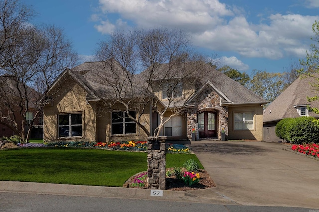 traditional-style home featuring a front yard, an attached garage, stone siding, driveway, and roof with shingles