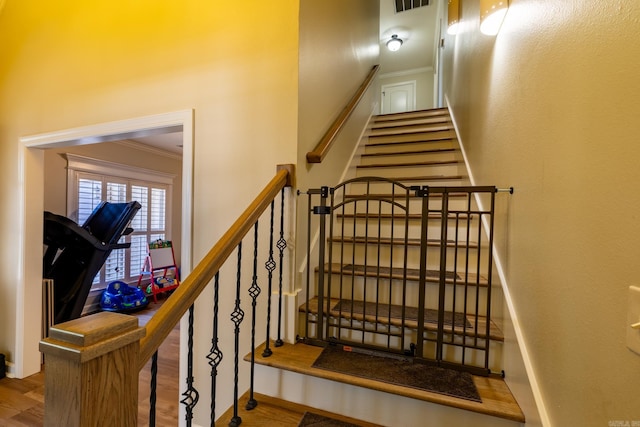 stairway with wood finished floors, baseboards, ornamental molding, and visible vents