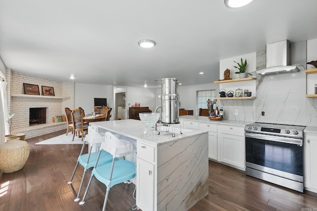 kitchen with stainless steel electric range oven, open shelves, wall chimney range hood, open floor plan, and white cabinetry