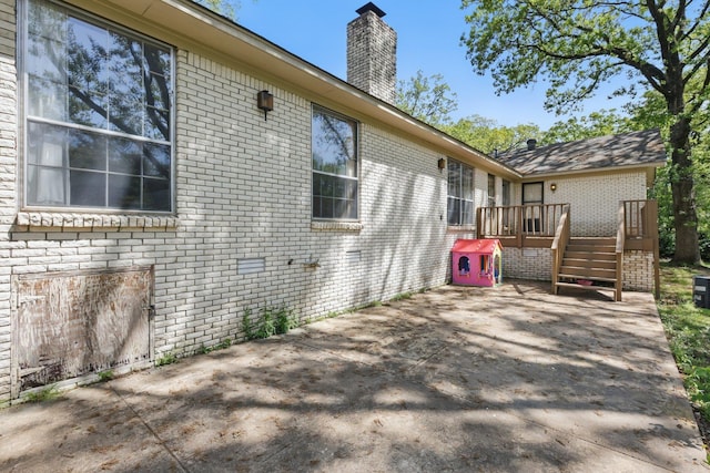 view of side of property with brick siding, a wooden deck, a patio, and a chimney
