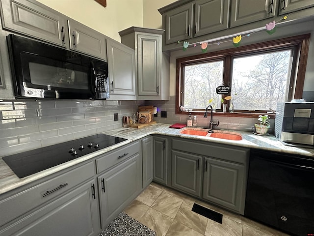 kitchen with gray cabinets, decorative backsplash, a sink, and black appliances