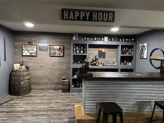 bar with a textured wall, wooden walls, a dry bar, and wood finished floors