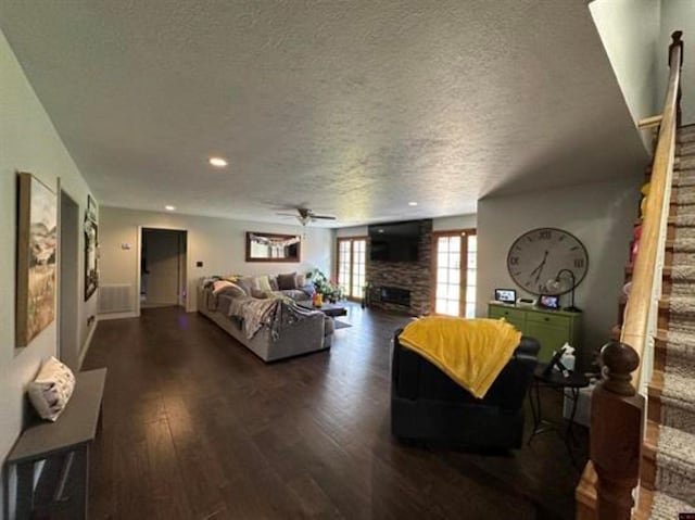 living area with dark wood-type flooring, a textured ceiling, a ceiling fan, and a fireplace