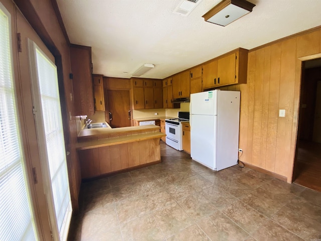 817 Waco St, Camden, AR 71701 - kitchen with white appliances, a sink, wood walls, under cabinet range hood, and brown cabinetry