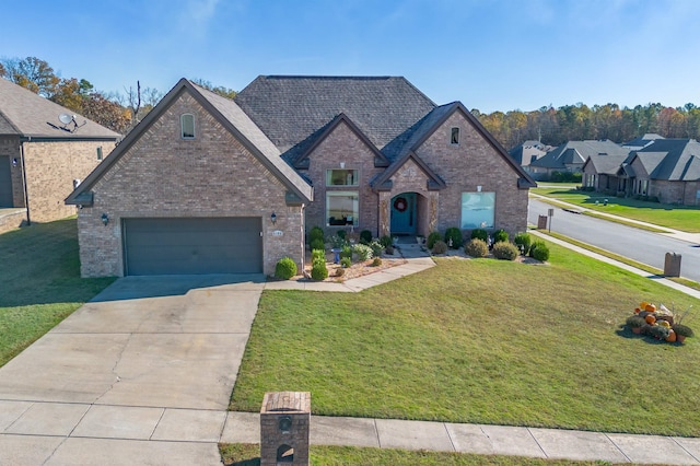 french provincial home with a garage, concrete driveway, brick siding, and a front yard