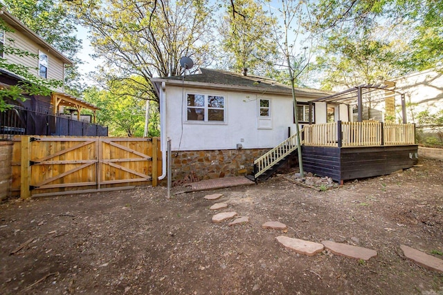 rear view of property with fence, stucco siding, a deck, and a gate