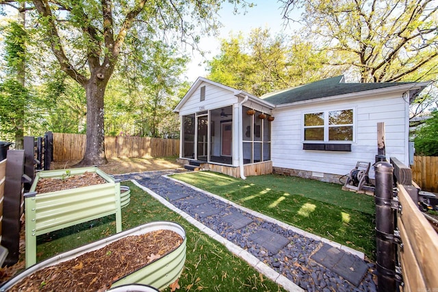 rear view of house with a vegetable garden, a sunroom, crawl space, a yard, and a fenced backyard