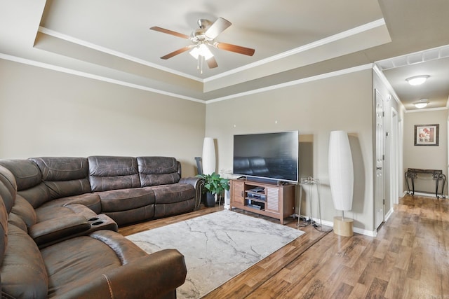 living area featuring light wood-type flooring, a ceiling fan, a tray ceiling, and ornamental molding