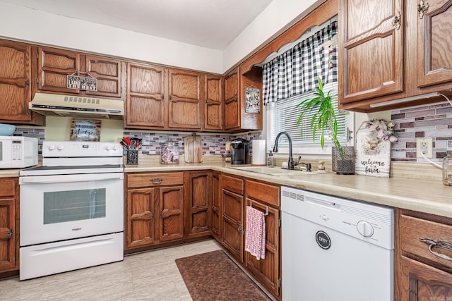 kitchen featuring under cabinet range hood, white appliances, a sink, and tasteful backsplash