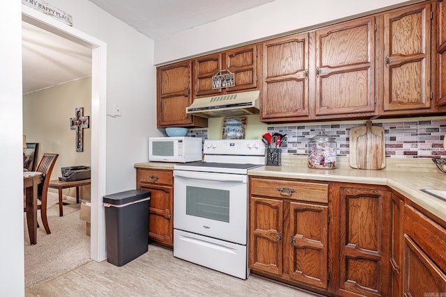 kitchen with under cabinet range hood, white appliances, brown cabinets, and backsplash