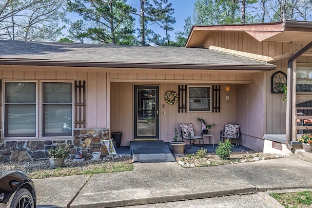 property entrance with a porch, stone siding, and roof with shingles