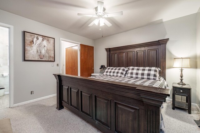 bedroom featuring ensuite bath, light colored carpet, baseboards, and ceiling fan
