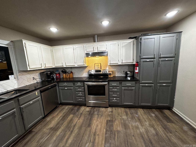 kitchen featuring stainless steel appliances, dark wood finished floors, under cabinet range hood, and dark countertops