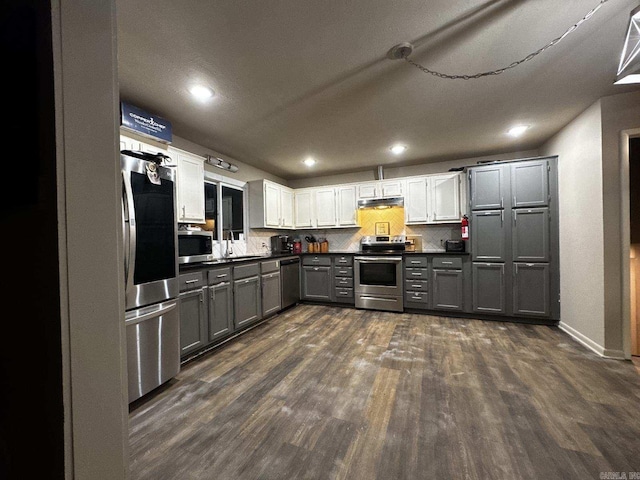 kitchen with a sink, dark countertops, stainless steel appliances, gray cabinetry, and dark wood-style floors