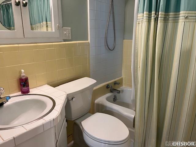 bathroom featuring toilet, tile walls, vanity, and shower / bath combination with curtain