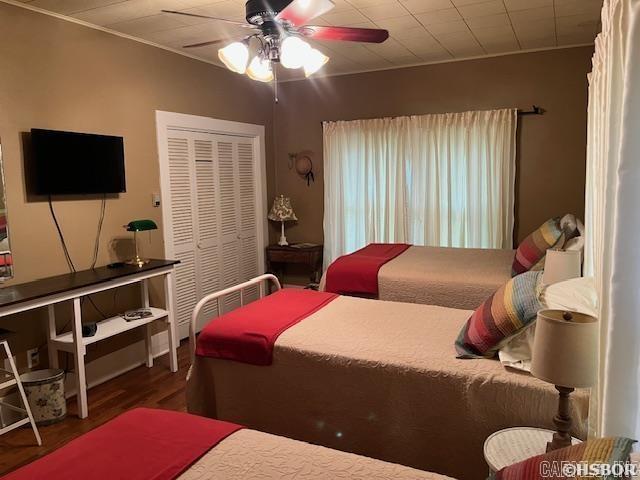 bedroom with ceiling fan, a closet, crown molding, and wood finished floors
