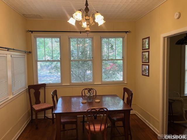 dining room with ornamental molding, an inviting chandelier, baseboards, and dark wood-style floors