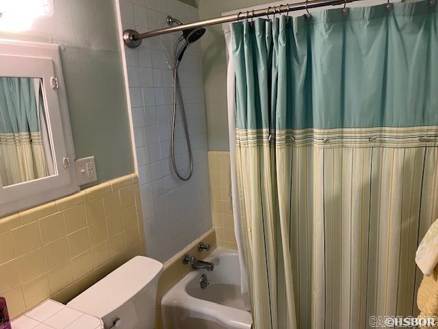 full bathroom with toilet, tile walls, and shower / bath combo with shower curtain