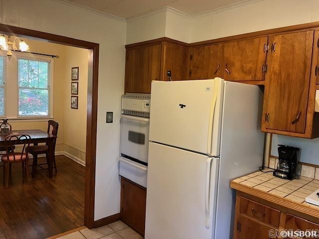 kitchen with a warming drawer, white appliances, brown cabinetry, and tile counters