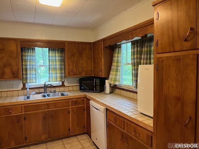 kitchen featuring black microwave, a wealth of natural light, white dishwasher, tile countertops, and a sink