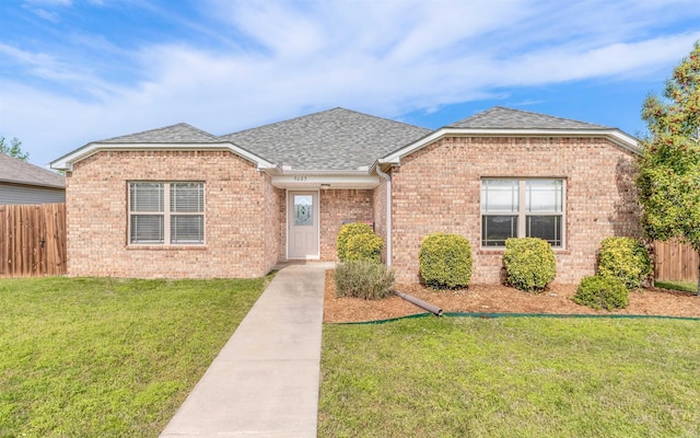 single story home featuring roof with shingles, fence, a front lawn, and brick siding