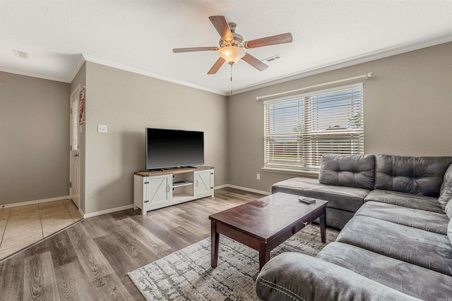 living area featuring light wood-style flooring, ornamental molding, a ceiling fan, visible vents, and baseboards