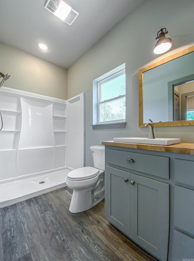 full bathroom featuring wood finished floors, vanity, a shower, toilet, and visible vents