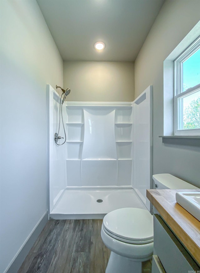 bathroom featuring wood finished floors, toilet, vanity, baseboards, and a stall shower