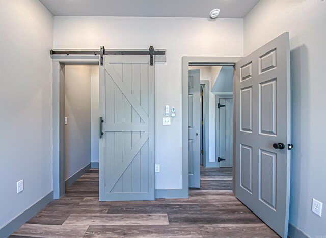 unfurnished bedroom with a barn door, wood finished floors, and baseboards