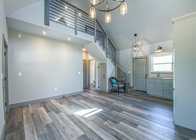 unfurnished living room featuring an inviting chandelier, wood finished floors, stairs, a sink, and high vaulted ceiling