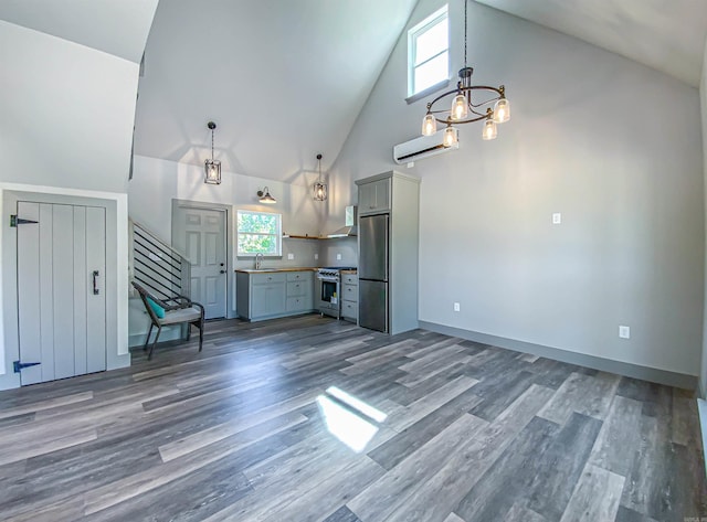 unfurnished living room with high vaulted ceiling, stairway, wood finished floors, a notable chandelier, and a wall unit AC
