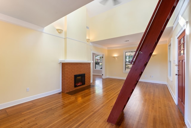 unfurnished living room featuring a fireplace, light wood finished floors, a towering ceiling, and baseboards
