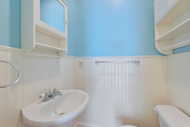 half bath featuring a sink, toilet, a decorative wall, and wainscoting
