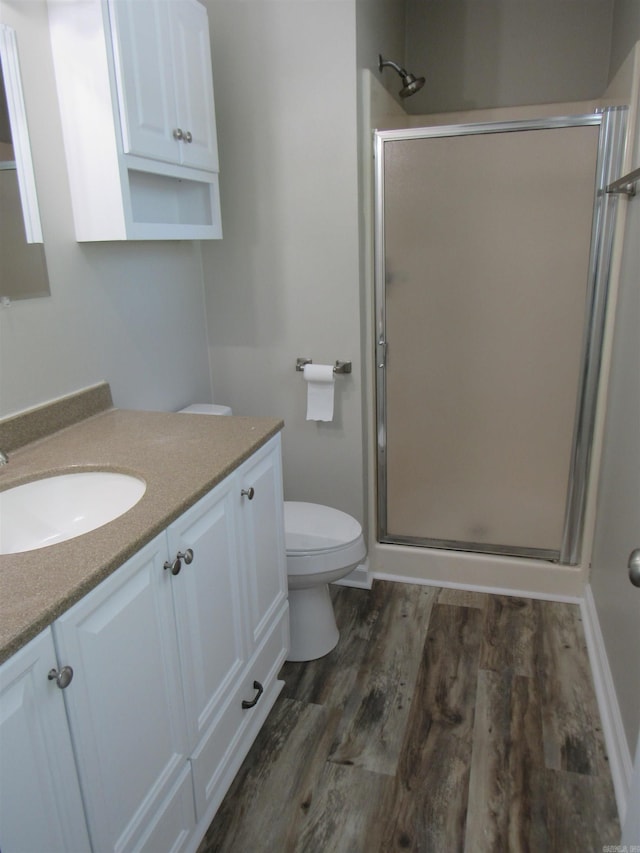 full bath with toilet, vanity, a stall shower, and wood finished floors