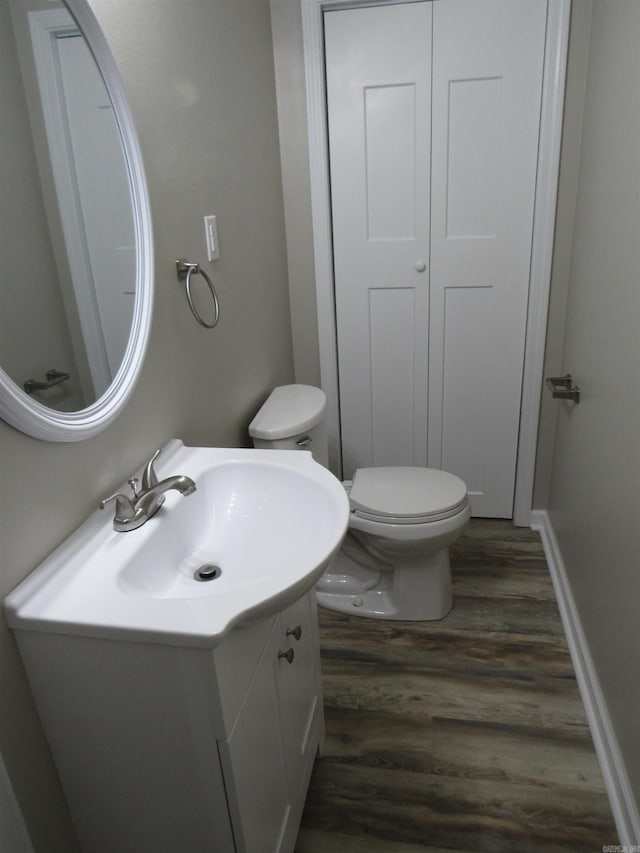 half bath featuring toilet, wood finished floors, vanity, and baseboards