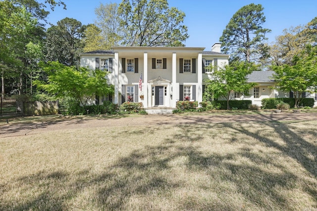 neoclassical home with a front lawn, stucco siding, and a chimney