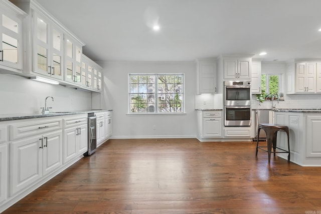 kitchen with white cabinets, double oven, recessed lighting, dark wood-type flooring, and beverage cooler