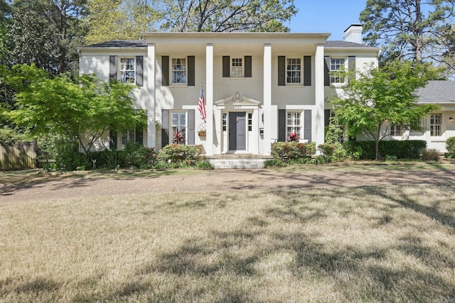 greek revival inspired property featuring a chimney and a front lawn