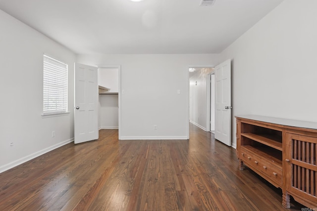 unfurnished bedroom with a spacious closet, dark wood-style floors, baseboards, and visible vents