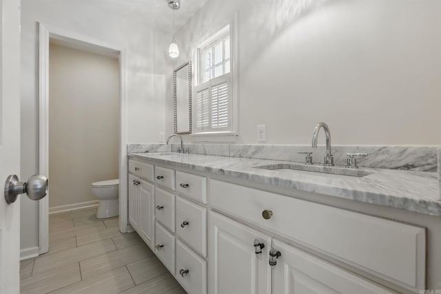 bathroom featuring a sink, toilet, double vanity, and baseboards