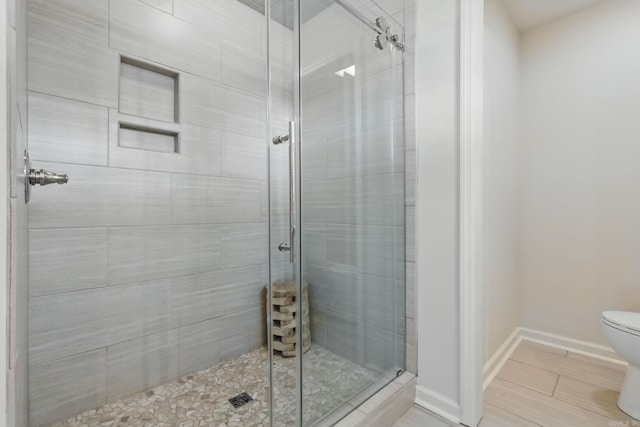 bathroom featuring toilet, a stall shower, and baseboards