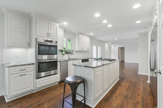 kitchen with a center island, dark wood-style flooring, a sink, stainless steel appliances, and backsplash